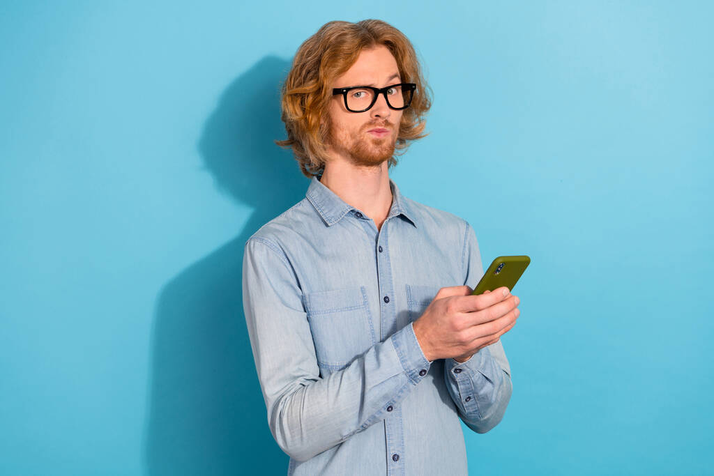 Фото мыслящего серьезного человека держать телефон угрюмое лицо хм глубоко изолированы на синем фоне цвета. - Фото, изображение