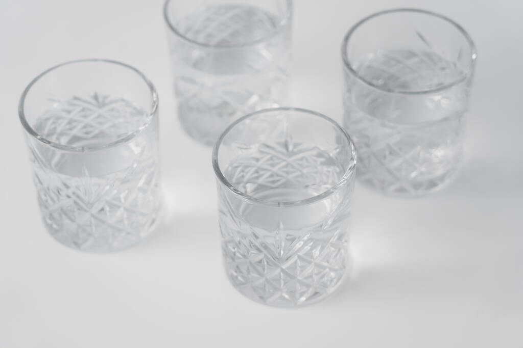 vista ad alto angolo di acqua in bicchieri con motivo sfaccettato sulla superficie bianca - Foto, immagini