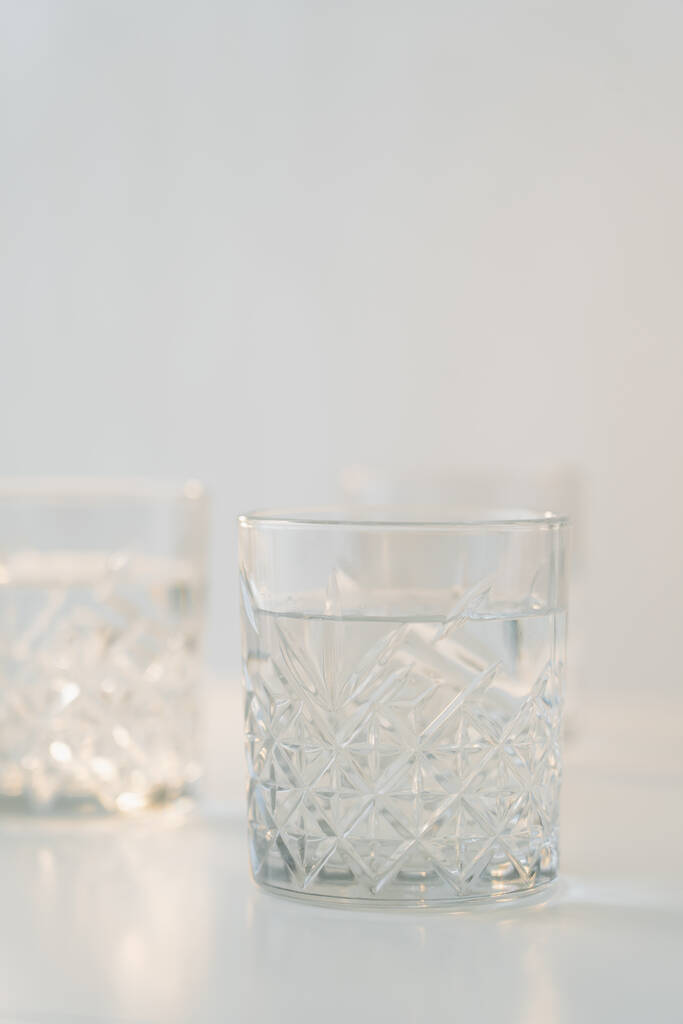 glas met geslepen patroon en zuiver water op grijze wazige ondergrond - Foto, afbeelding