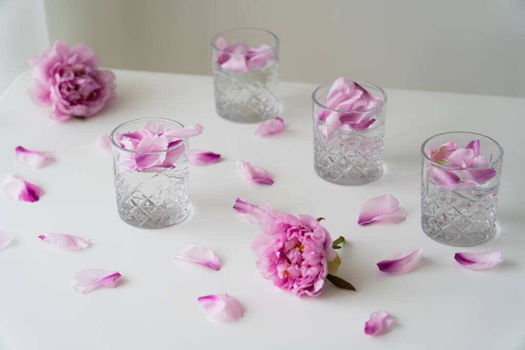 白いテーブルの上にピンク色の牡丹の近くに強壮剤と花の花びらのメガネとグレーの背景 - 写真・画像