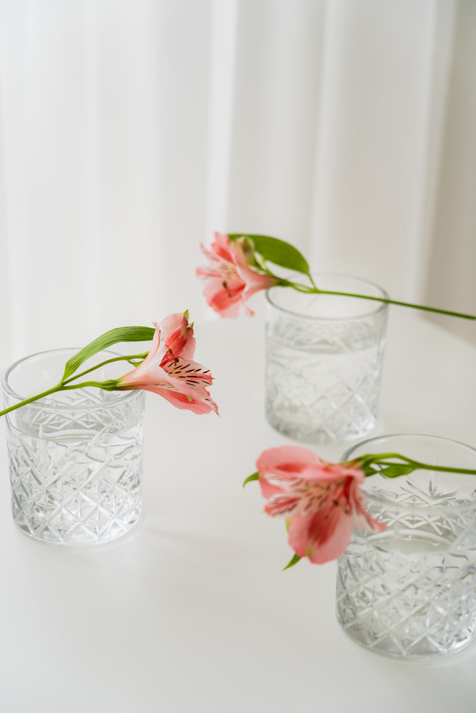 vasos de cristal con agua cerca de flores de alstroemeria sobre mesa blanca y fondo gris - Foto, Imagen