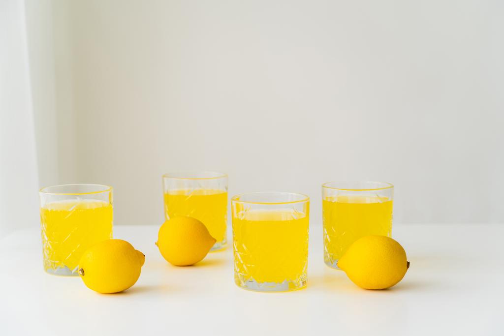 hele citroenen bij glazen met zuiver citrussap op grijze achtergrond met kopieerruimte - Foto, afbeelding