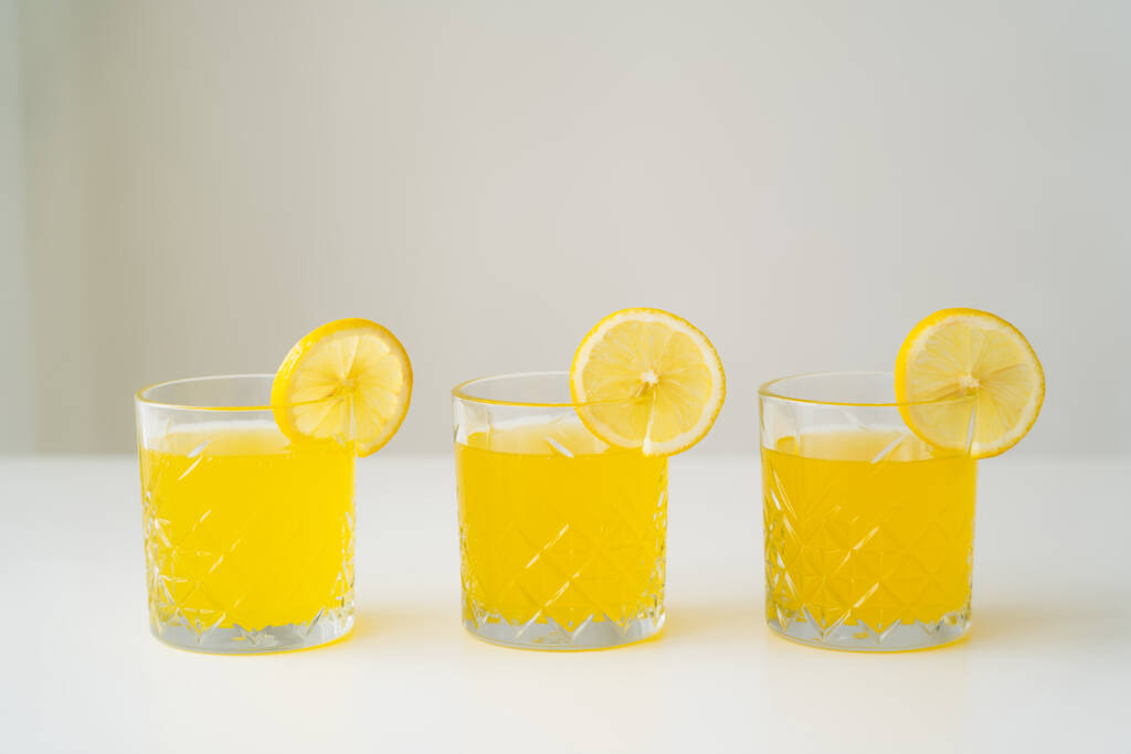 plátky čerstvého citronu na sklenicích s přírodní citrusovou šťávou na bílém povrchu izolované na šedé - Fotografie, Obrázek