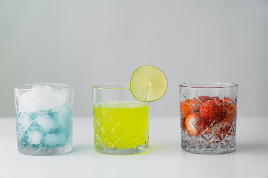 lemonade and strawberry tonic near glass with ice cubes on white surface isolated on grey - Photo, Image