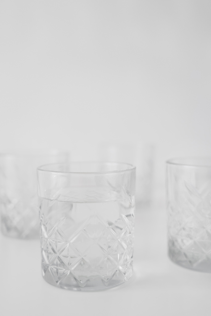 selektiver Fokus aus transparentem Glas mit Wasser auf grauem, verschwommenem Hintergrund - Foto, Bild