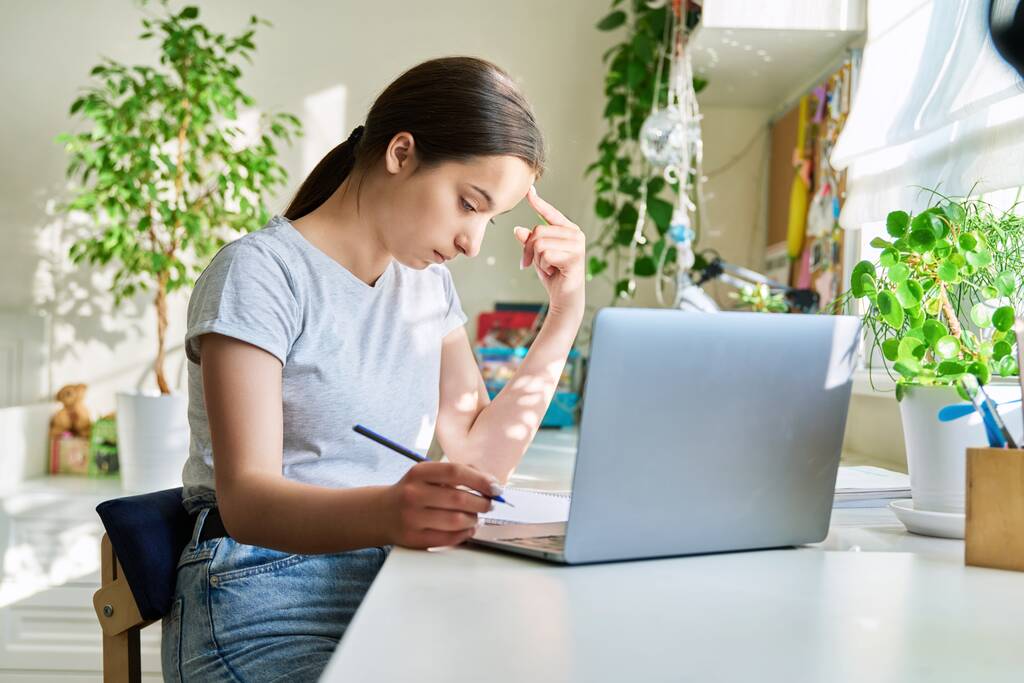 Adolescente étudiant à la maison à la table en utilisant un ordinateur portable. Étudiant adolescent étudiant en ligne faisant des devoirs en écrivant dans un ordinateur portable en regardant une leçon vidéo d'écoute. E-learning, adolescence, lycée, technologie - Photo, image