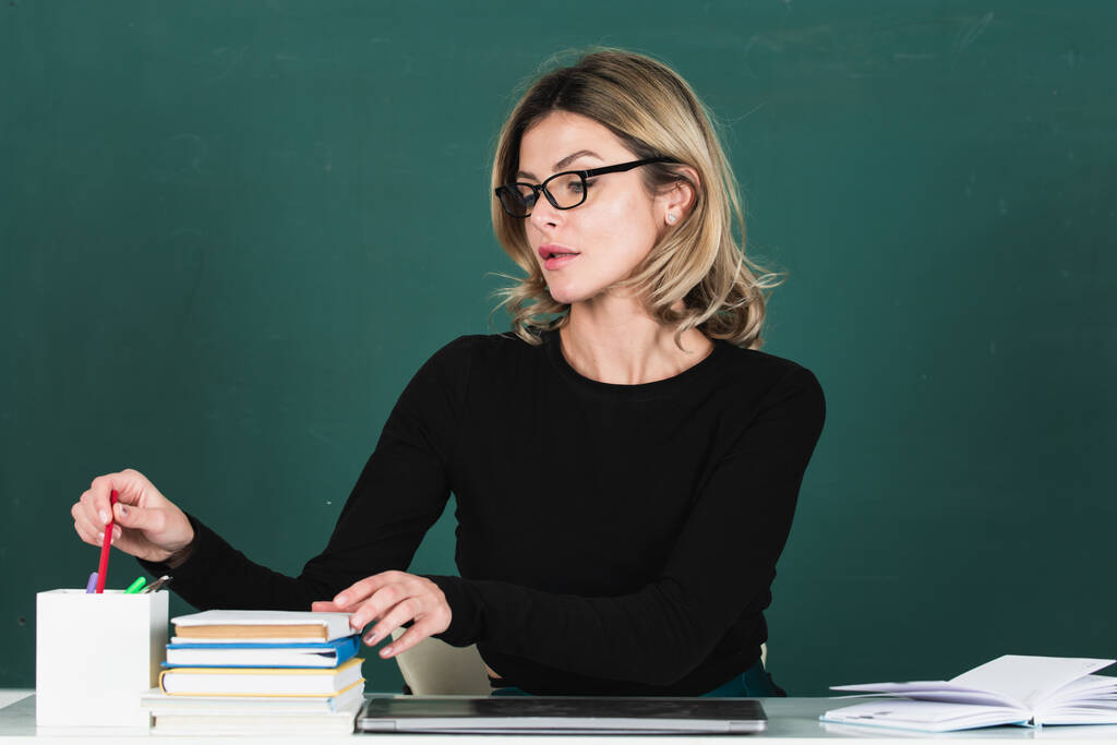Professor atraente moderno. Retrato de mulher jovem inteligente em óculos com livro no quadro-negro em sala de aula no ensino médio ou colagem. Conceito de educação e tutoria - Foto, Imagem