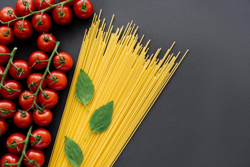Widok z góry dojrzałych pomidorów wiśniowych w pobliżu spaghetti i bazylii na czarnym tle  - Zdjęcie, obraz