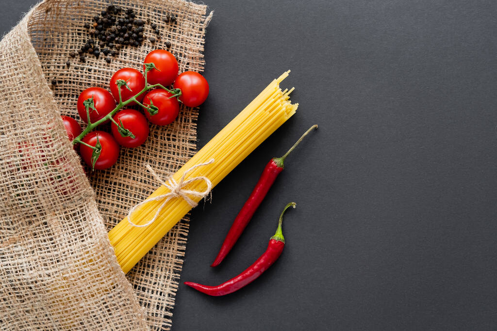 Widok z góry pomidory wiśniowe i papryka chili w pobliżu spaghetti na worek na czarnym tle  - Zdjęcie, obraz