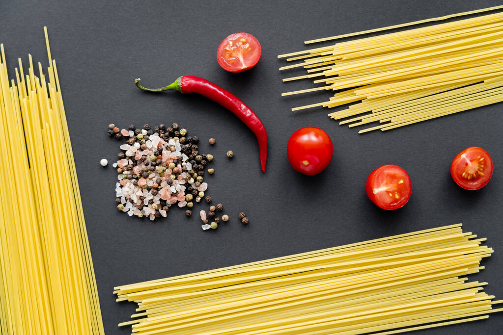 Bovenaanzicht van groenten met rauwe spaghetti en specerijen op zwarte achtergrond  - Foto, afbeelding