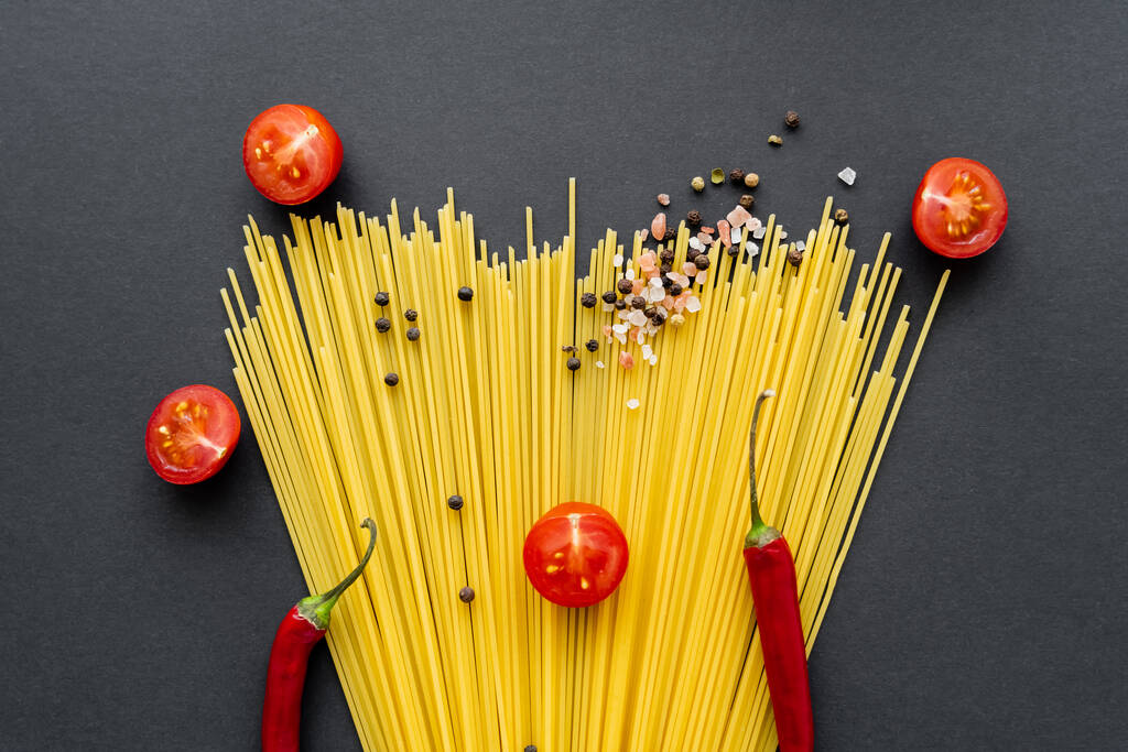 Flat lay of spices and chili peppers on raw spaghetti on black background  - Photo, Image