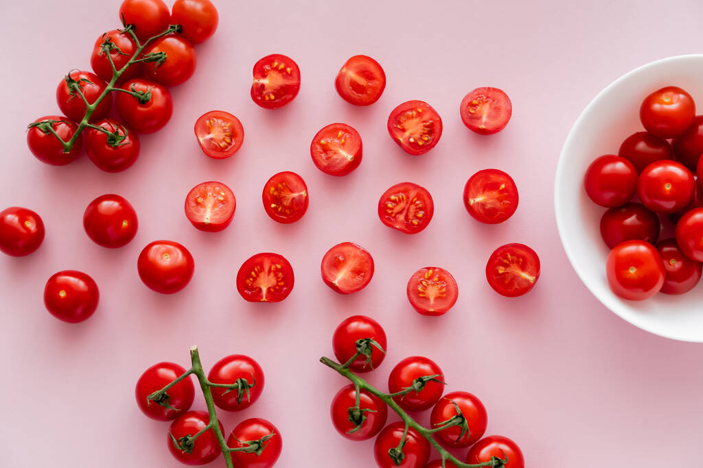 Vista superior de tomates cereja maduros na tigela e em ramos no fundo rosa  - Foto, Imagem