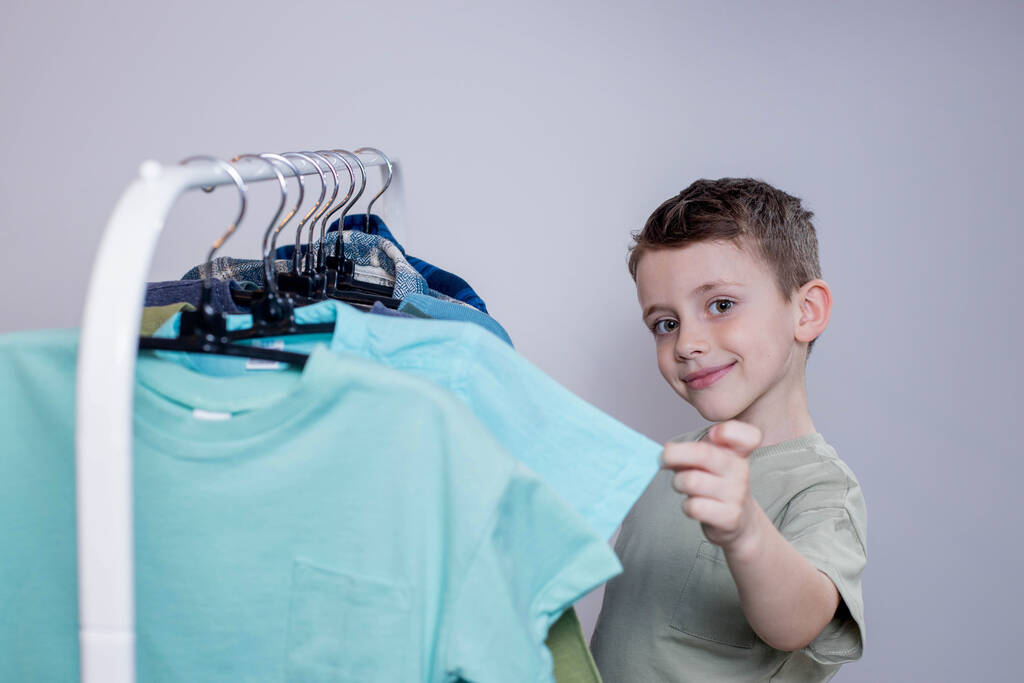 Boy preschooler standing by the hangers, racks up clothes, and chooses clothes for today. - Photo, Image