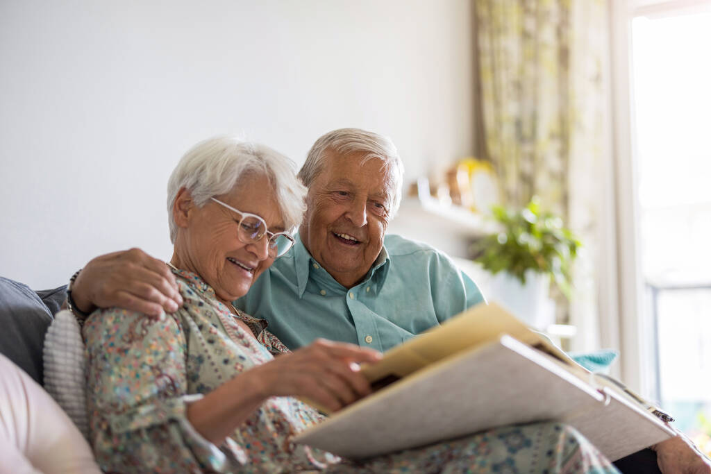 Casal de idosos olhando para um álbum de fotos enquanto sentado em um sofá - Foto, Imagem
