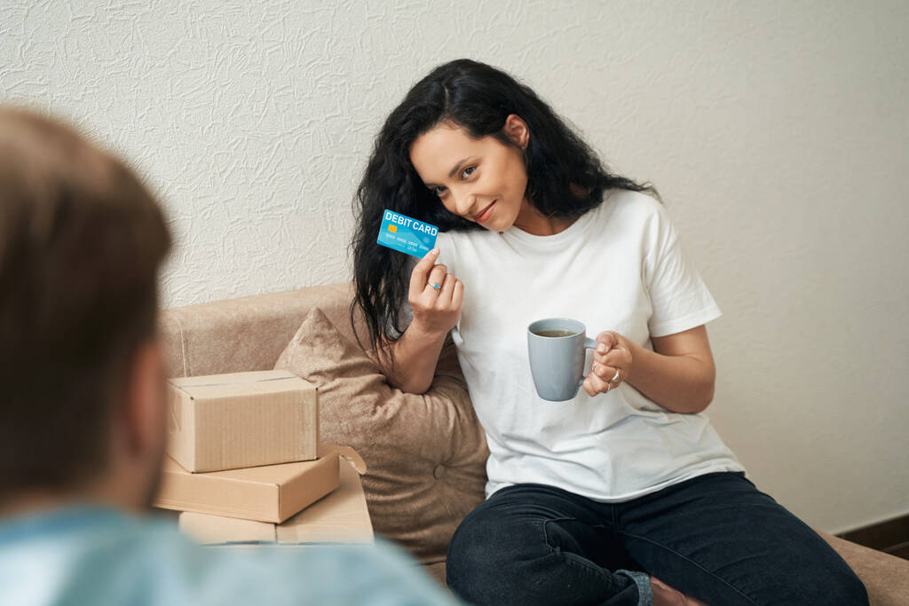 Mosolygó elégedett nő ül a kanapén, és mutatja betéti kártya a férfi - Fotó, kép