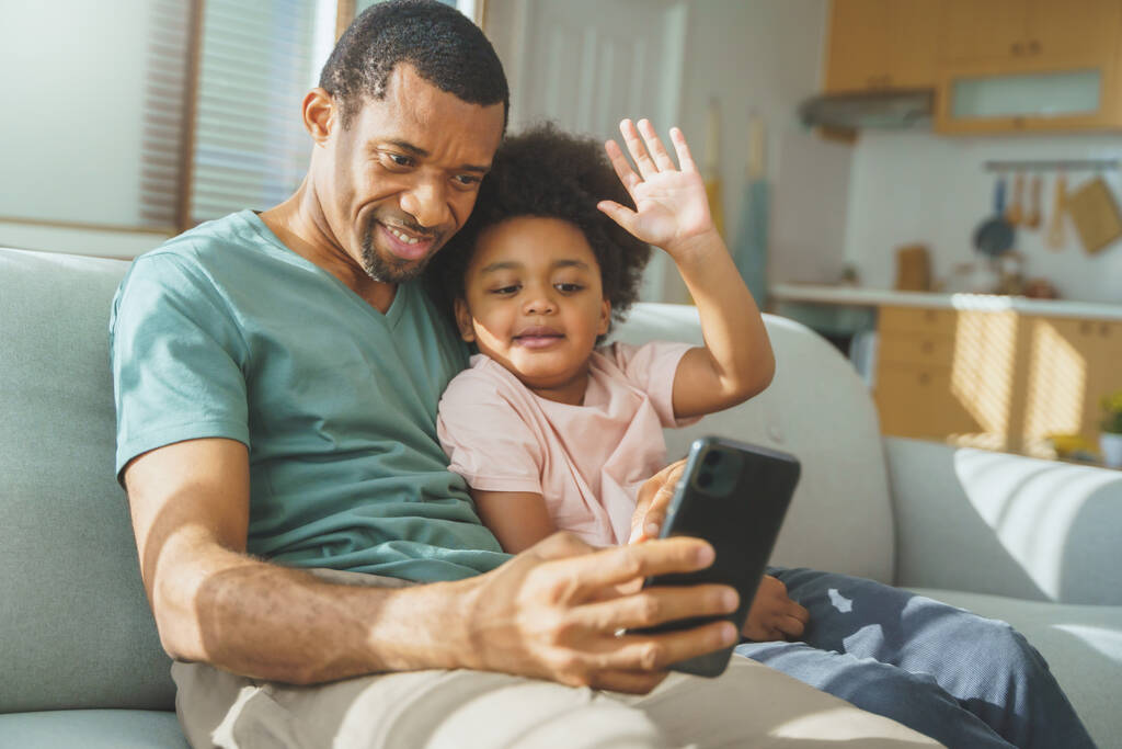 Afrikalı Amerikalı baba ve mutlu çocuk cep telefonuyla görüntülü konuşma yapıyor, Siyah Baba ve oğlu kanepeye oturmuş selfie çekiyor.. - Fotoğraf, Görsel