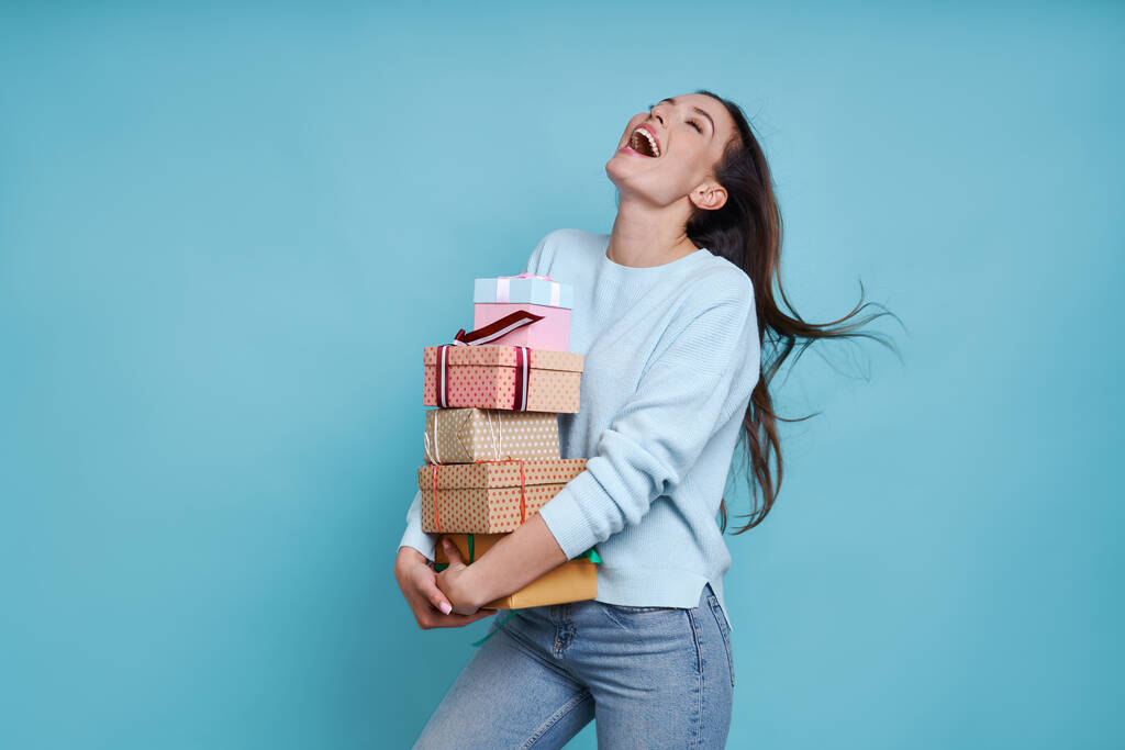 Aufgeregte junge Frau mit vielen Geschenkboxen vor blauem Hintergrund - Foto, Bild