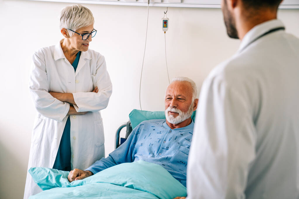 Az orvos egy idős férfi beteggel beszél a kórházi ágyban, aki lábadozik a betegségből. Egészségügyi ellátás, coronavirus, emberek koncepciója. - Fotó, kép
