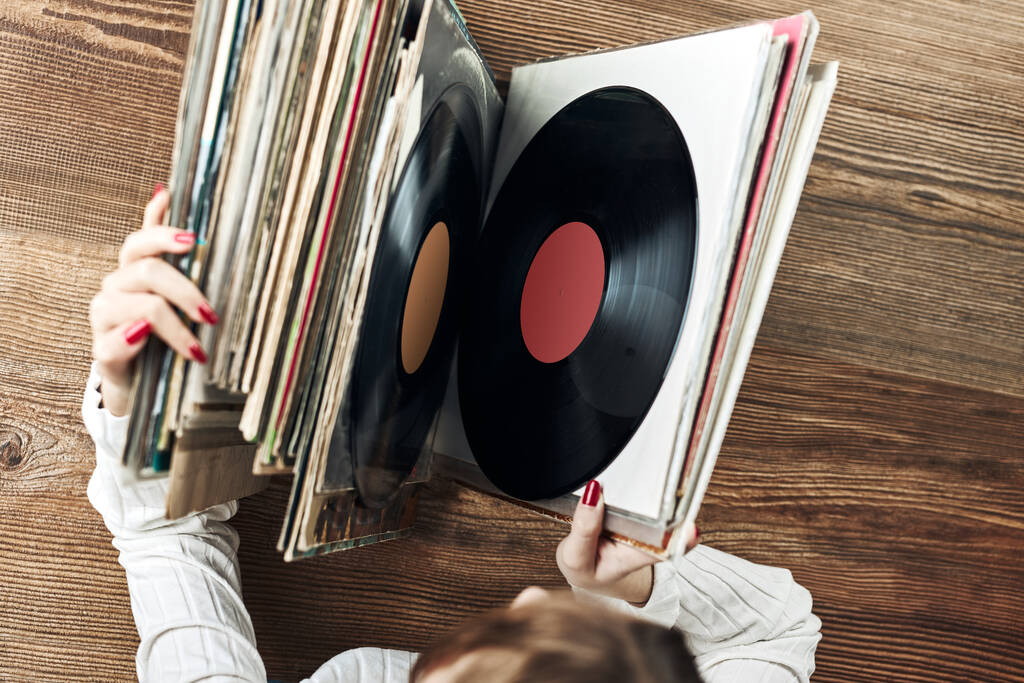 Playing vinyl records. Listening to music from vinyl record player. Retro and vintage music style. Woman holding analog LP record album. Stack of old records. Music collection. Music passion - Foto, Bild