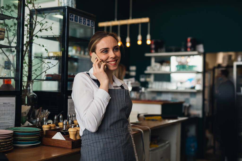 жінка офіціантка розмовляє з мобільним телефоном в ресторані
 - Фото, зображення