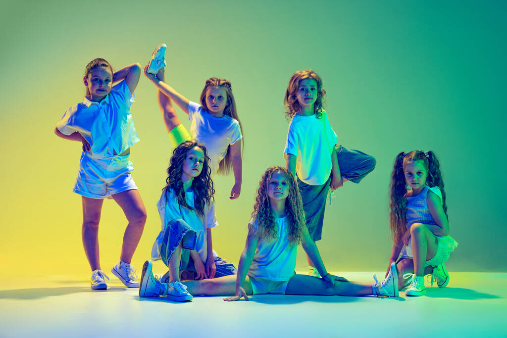 Futuros bailarinos desprezíveis. Grupo de crianças, meninas em roupas esportivas estilo casual dançando na aula de coreografia isolado em fundo verde em luz de néon. Conceito de música, moda, arte - Foto, Imagem