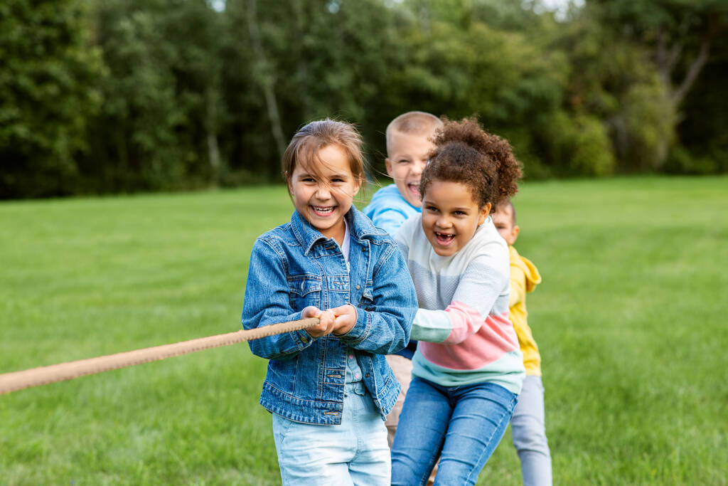 παιδική ηλικία, αναψυχή και άνθρωποι έννοια - ομάδα ευτυχισμένων παιδιών που παίζουν ρυμουλκό-of-war παιχνίδι και τρέχει στο πάρκο - Φωτογραφία, εικόνα