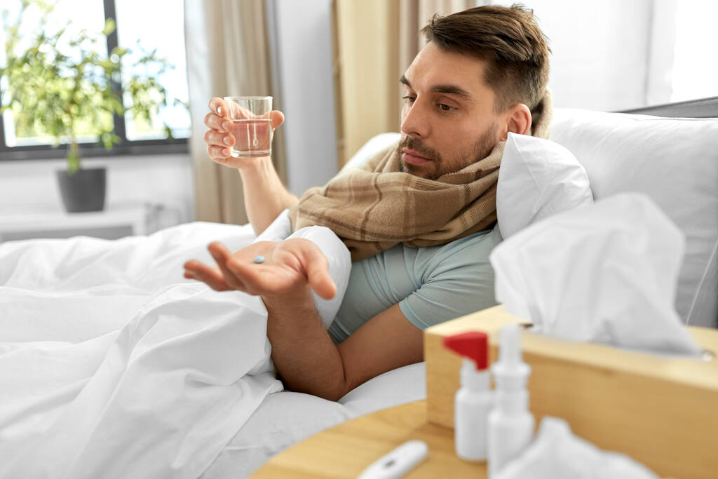 personas y el concepto de problemas de salud - hombre enfermo infeliz con píldora de la medicina y vaso de agua acostado en la cama en casa - Foto, Imagen
