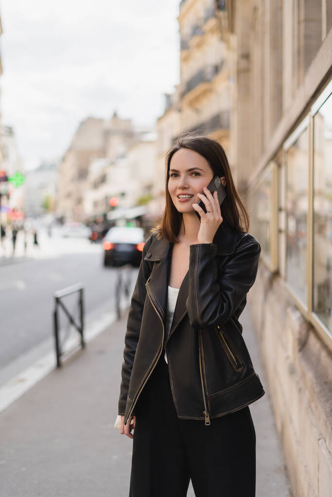 vrolijk jong vrouw in stijlvolle jas praten op smartphone op straat in Parijs  - Foto, afbeelding