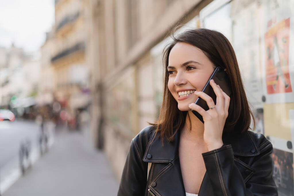retrato de la joven alegre en chaqueta elegante hablando en el teléfono inteligente en la calle en París  - Foto, Imagen