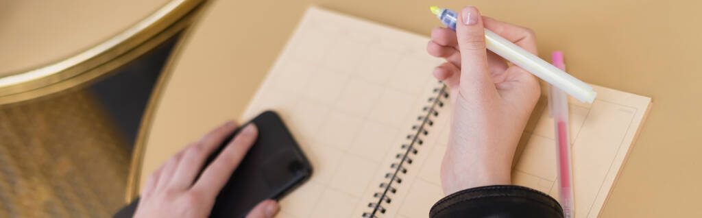 oříznutý pohled ženy držící tužku a smartphone u prázdného notebooku na kulatém stole, banner - Fotografie, Obrázek