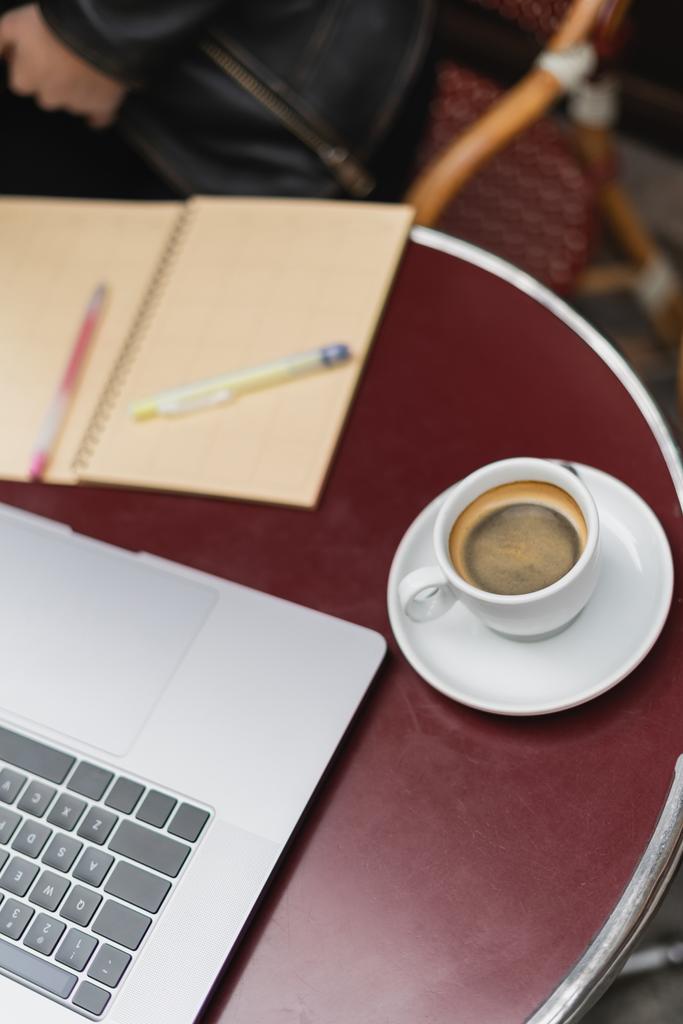 laptop és csésze kávé közelében elmosódott notebook az asztalon a szabadtéri kávézóban  - Fotó, kép