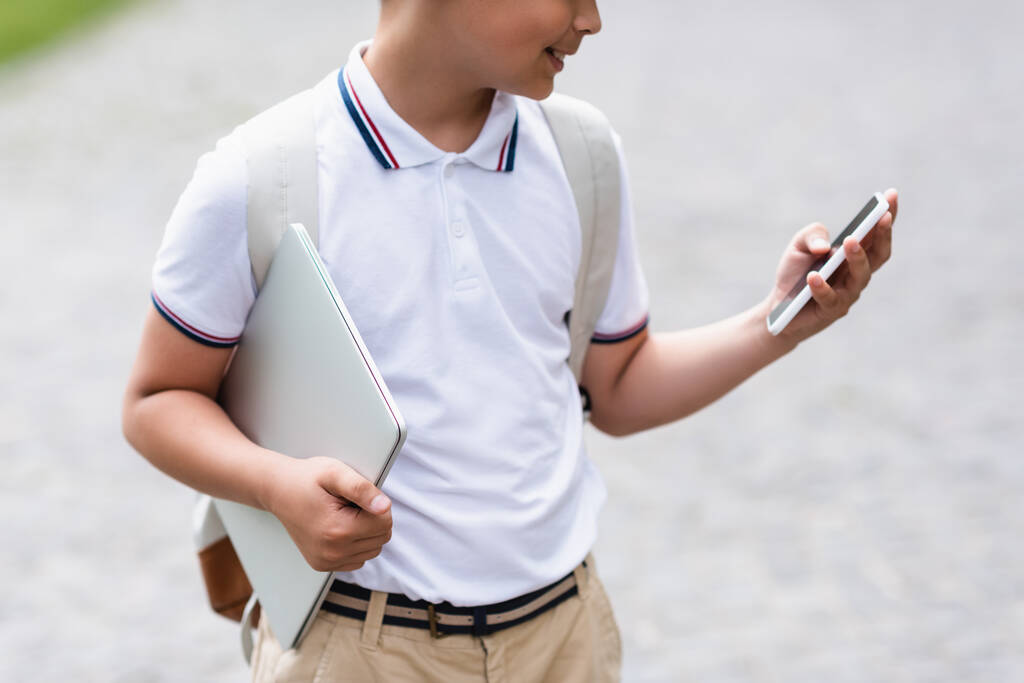 スマートフォンやノートパソコンを屋外に保持する学校の少年の作物ビュー  - 写真・画像