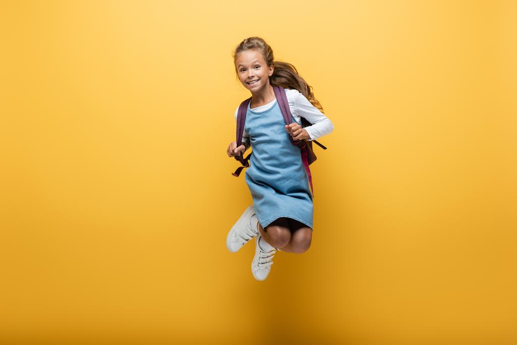 Щаслива дев'ятнадцять школярка з рюкзаком стрибає на жовтому тлі
 - Фото, зображення
