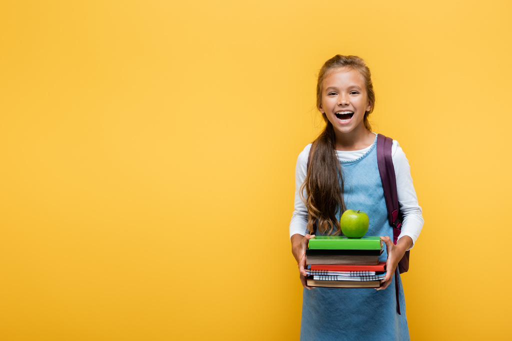 Fröhlicher Schüler hält Bücher und Apfel auf gelb  - Foto, Bild