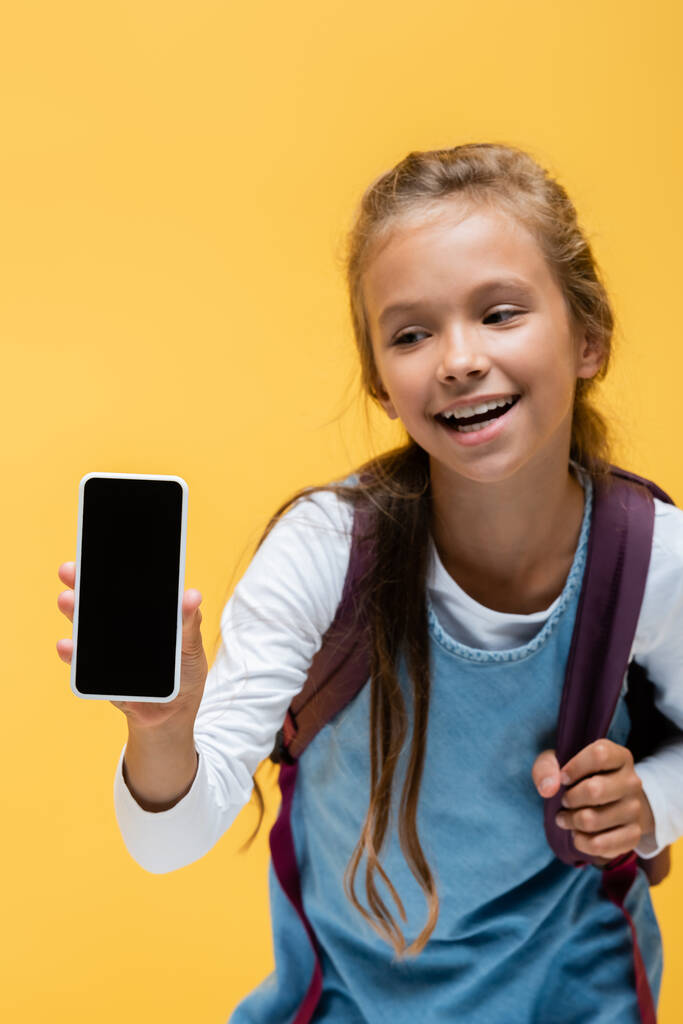 黄色に隔離された空白の画面と肯定的な小学生の保持バックパックとスマートフォン  - 写真・画像