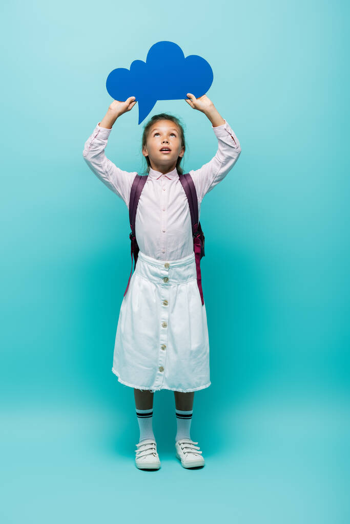 Full length of schoolgirl holding thought bubble on blue background  - Photo, Image