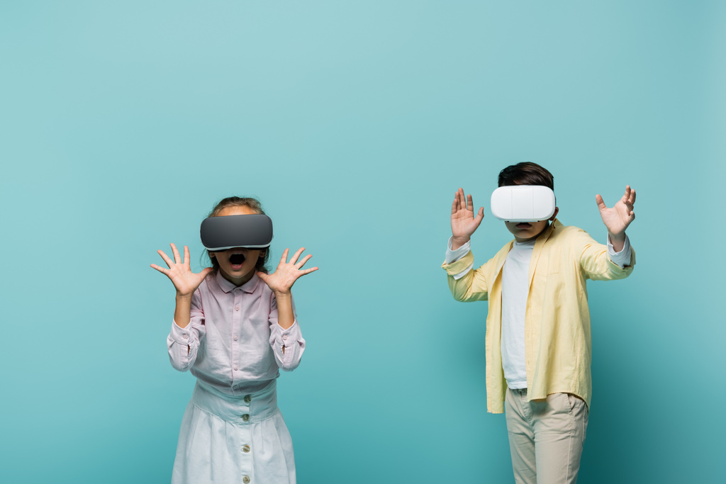 Scared kids in vr headsets gaming on blue background  - Photo, Image