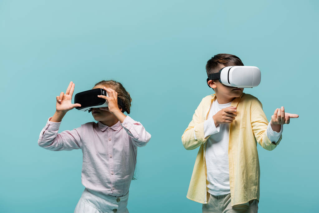 Preteen children in vr headsets playing video game and gesturing isolated on blue  - Photo, Image