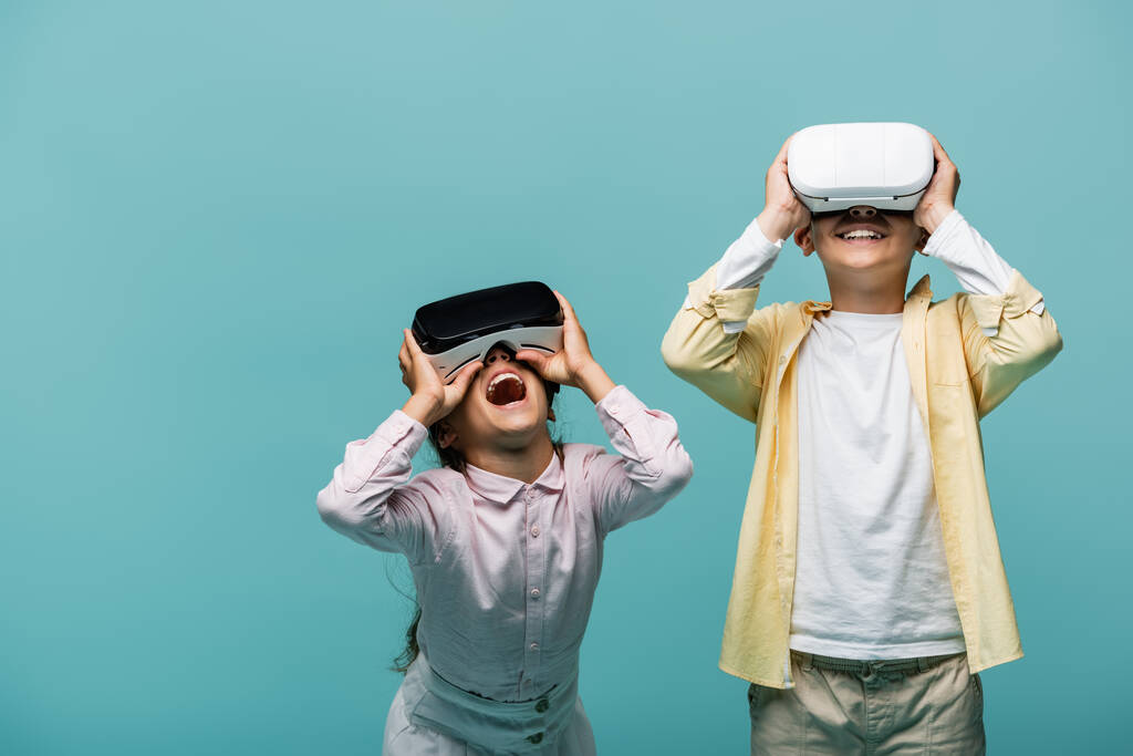 VR kulaklıklarıyla video oyunu oynayan heyecanlı çocuklar mavi renkte izole edilmiş.  - Fotoğraf, Görsel
