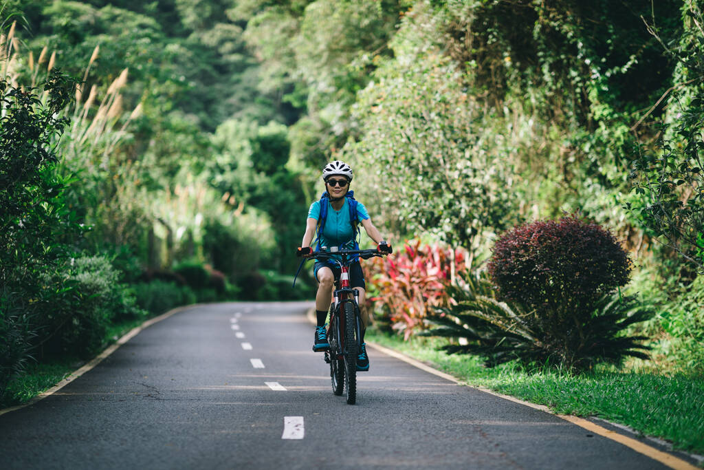 Жінка їде на велосипеді по тропічному парку влітку
 - Фото, зображення