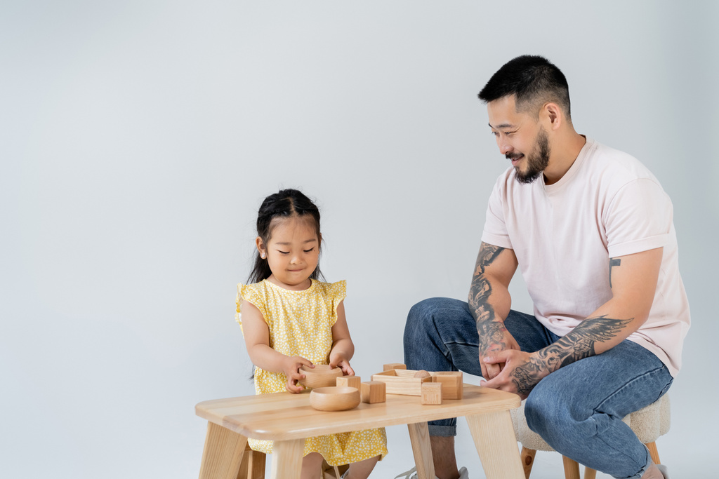 feliz asiático homem olhando morena filha brincando com madeira brinquedos isolado no cinza - Foto, Imagem