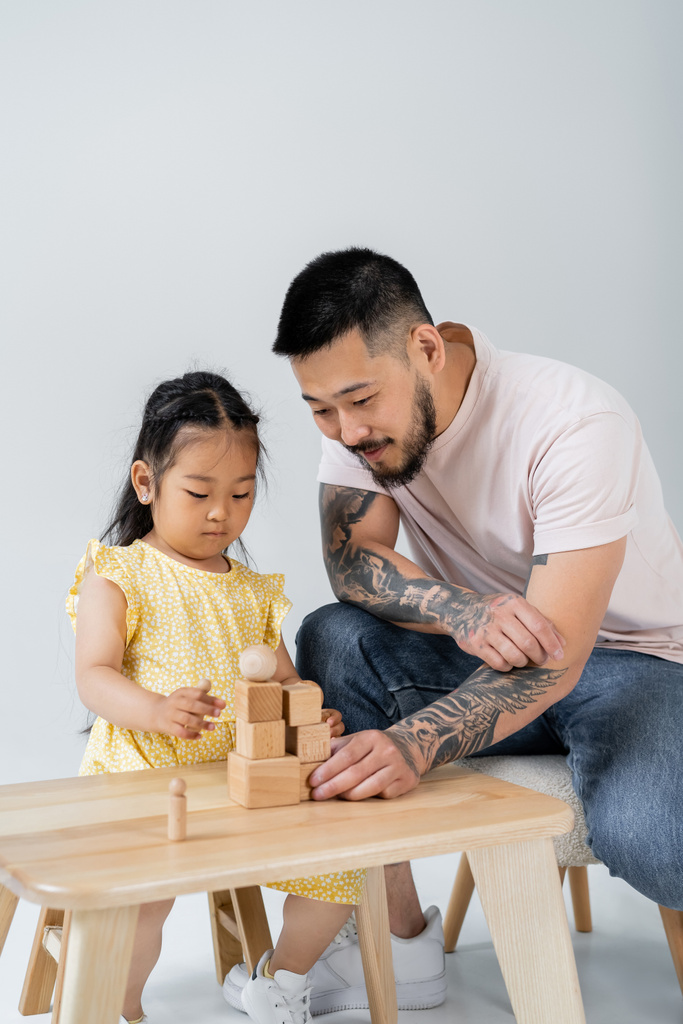 tattooed asian father playing wooden cubes with preschooler daughter isolated on grey - Photo, Image