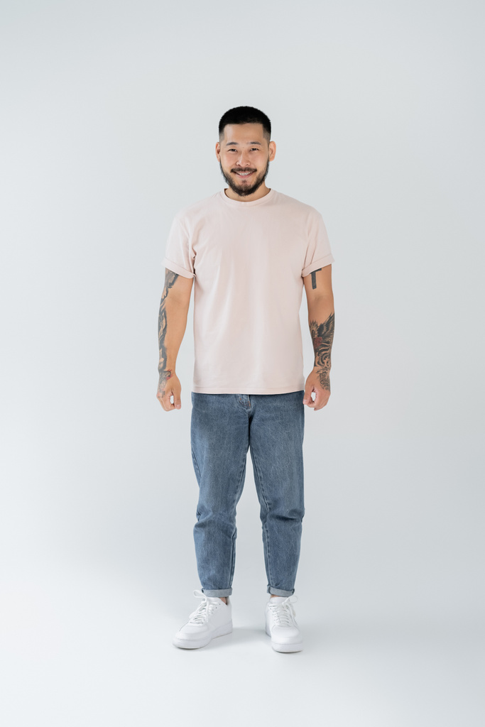 full length of happy asian man with beard standing in casual clothing on grey - Photo, Image