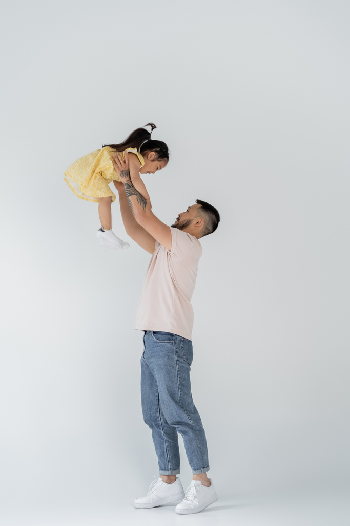 pleine longueur de asiatique homme lifting fille dans jaune robe sur gris - Photo, image