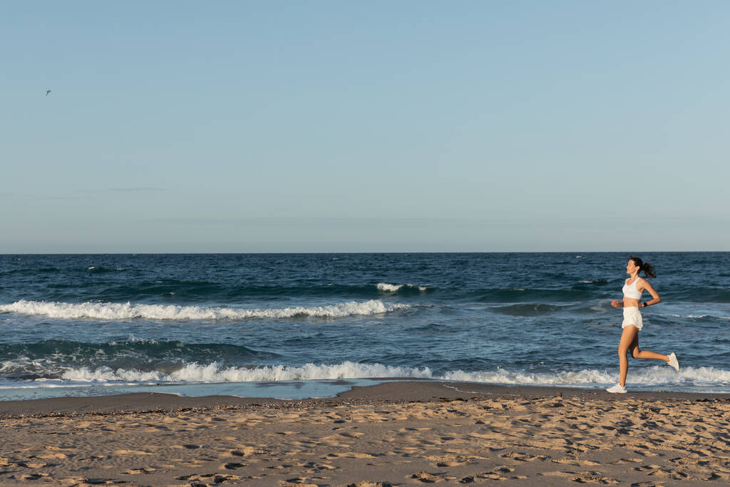 pełna długość młoda sportowa kobieta jogging w pobliżu morza w lecie - Zdjęcie, obraz