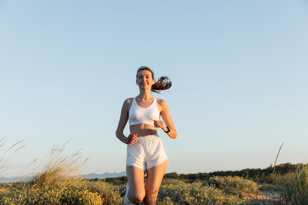 femme de sport heureuse en short et soutien-gorge de sport écouter de la musique et courir à l'extérieur  - Photo, image