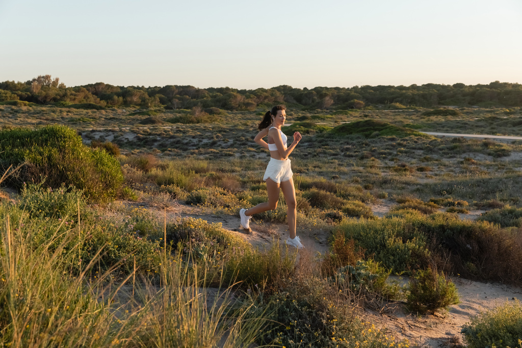 fitte Frau in kurzen Hosen und Sport-BH, die Musik hört und draußen rennt  - Foto, Bild