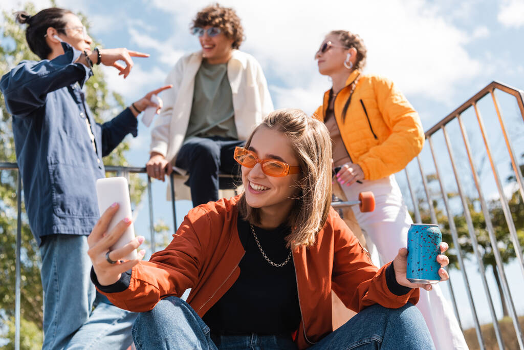 šťastná žena se sodou může užívat selfie v blízkosti multietnických přátel na rozmazaném pozadí - Fotografie, Obrázek
