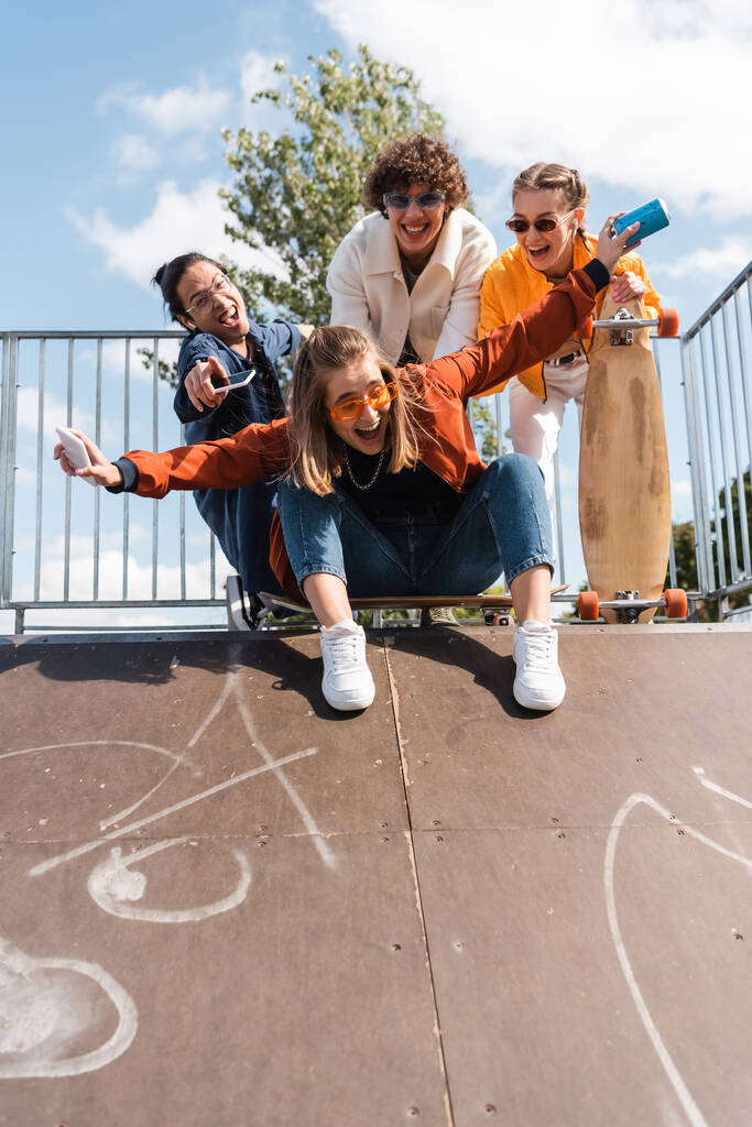 взволнованная женщина, кричащая на скейт-рампе рядом с улыбающимися межрасовыми друзьями - Фото, изображение