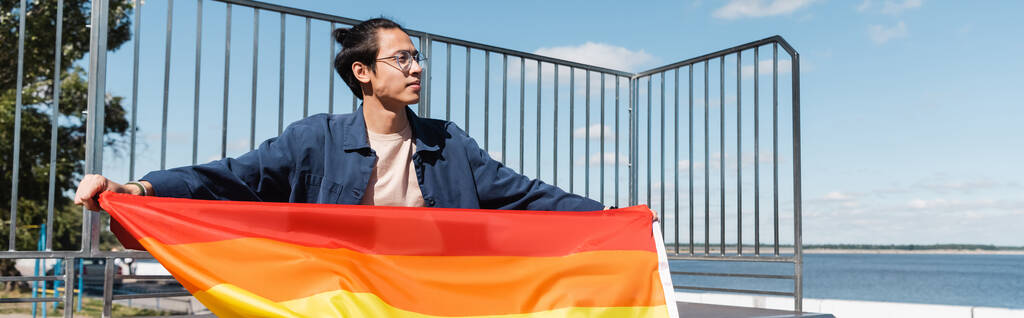 Asiat v brýlích držící vlajku Igbt a odvracející se pohled, prapor - Fotografie, Obrázek